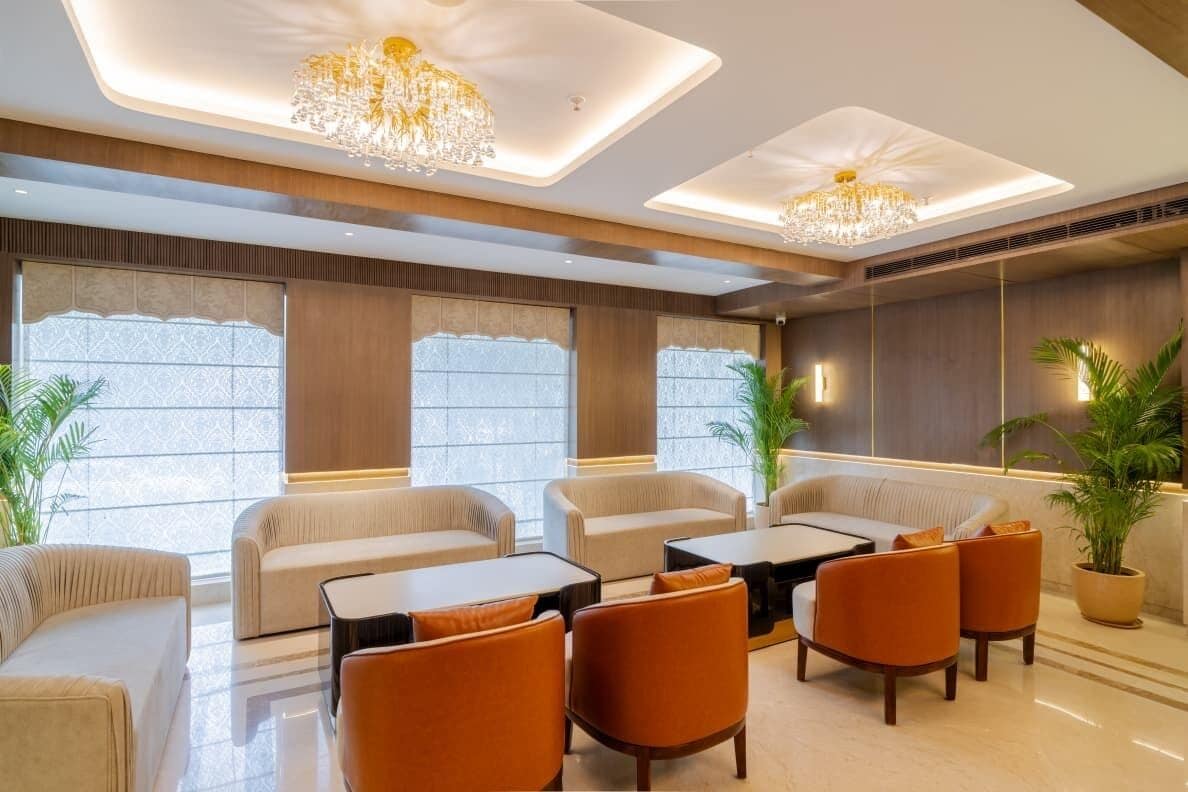 A modern lounge area with sofas, armchairs, and a coffee table, featuring a chandelier and large windows.