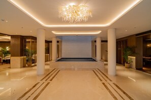 A spacious lobby with a central seating area, columns, and a chandelier. - AKS Palace (Varanasi)