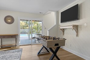 A room with a foosball table, a bench, a clock, and a television mounted on the wall. - SeaEsta | Private Pool + 5 Min Walk to Beach (Emerald Isle)