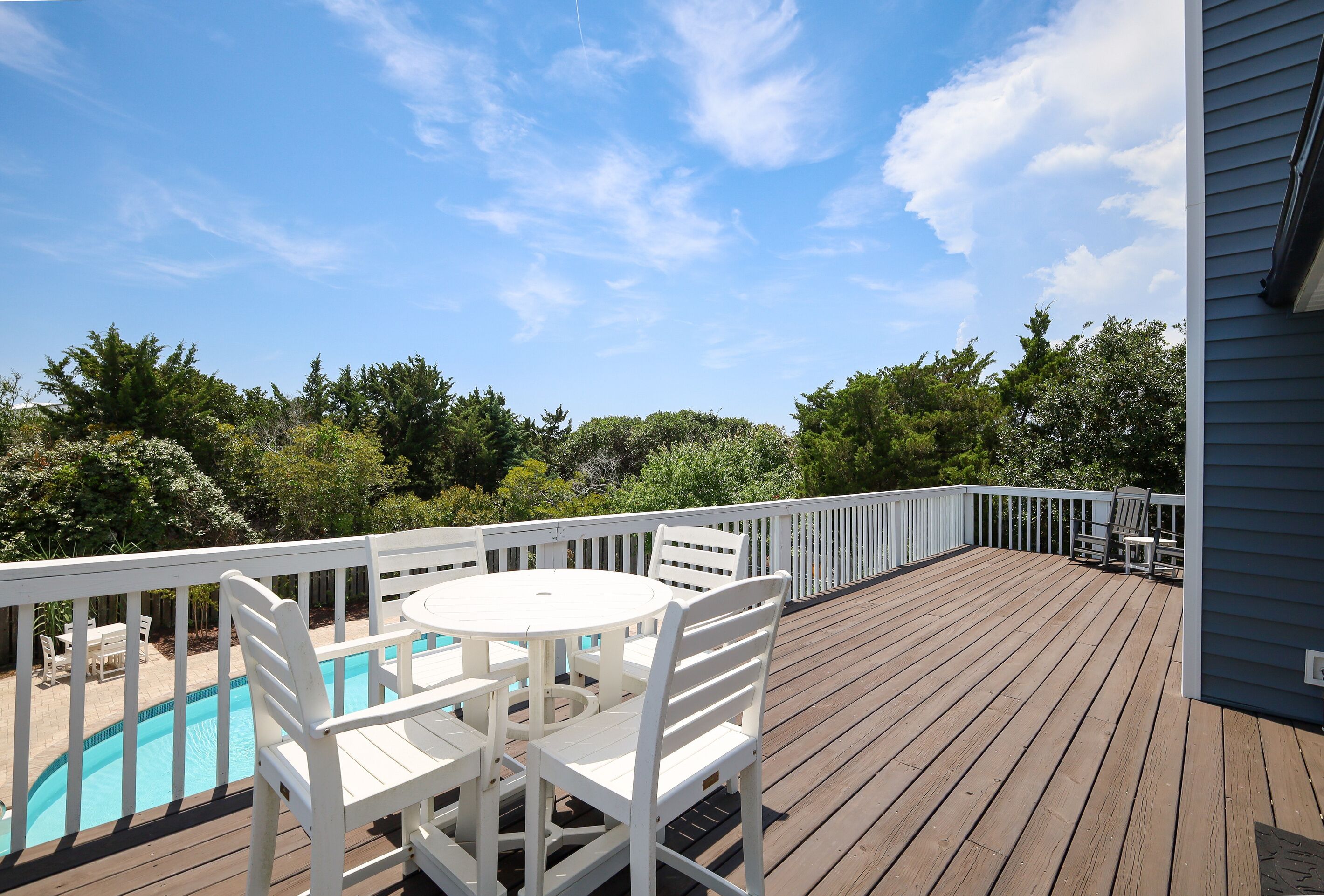 A wooden deck with a pool table and chairs, surrounded by a white railing.