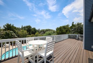 Um deck de madeira com mesa de bilhar e cadeiras, cercado por um corrimão branco.