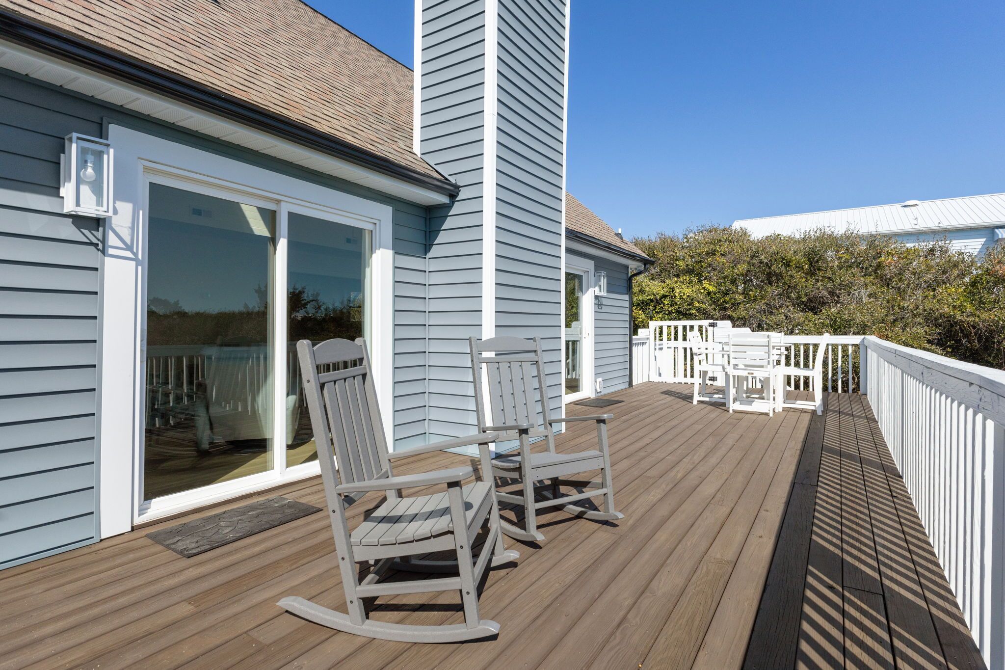 A wooden deck with two rocking chairs and a white fence.