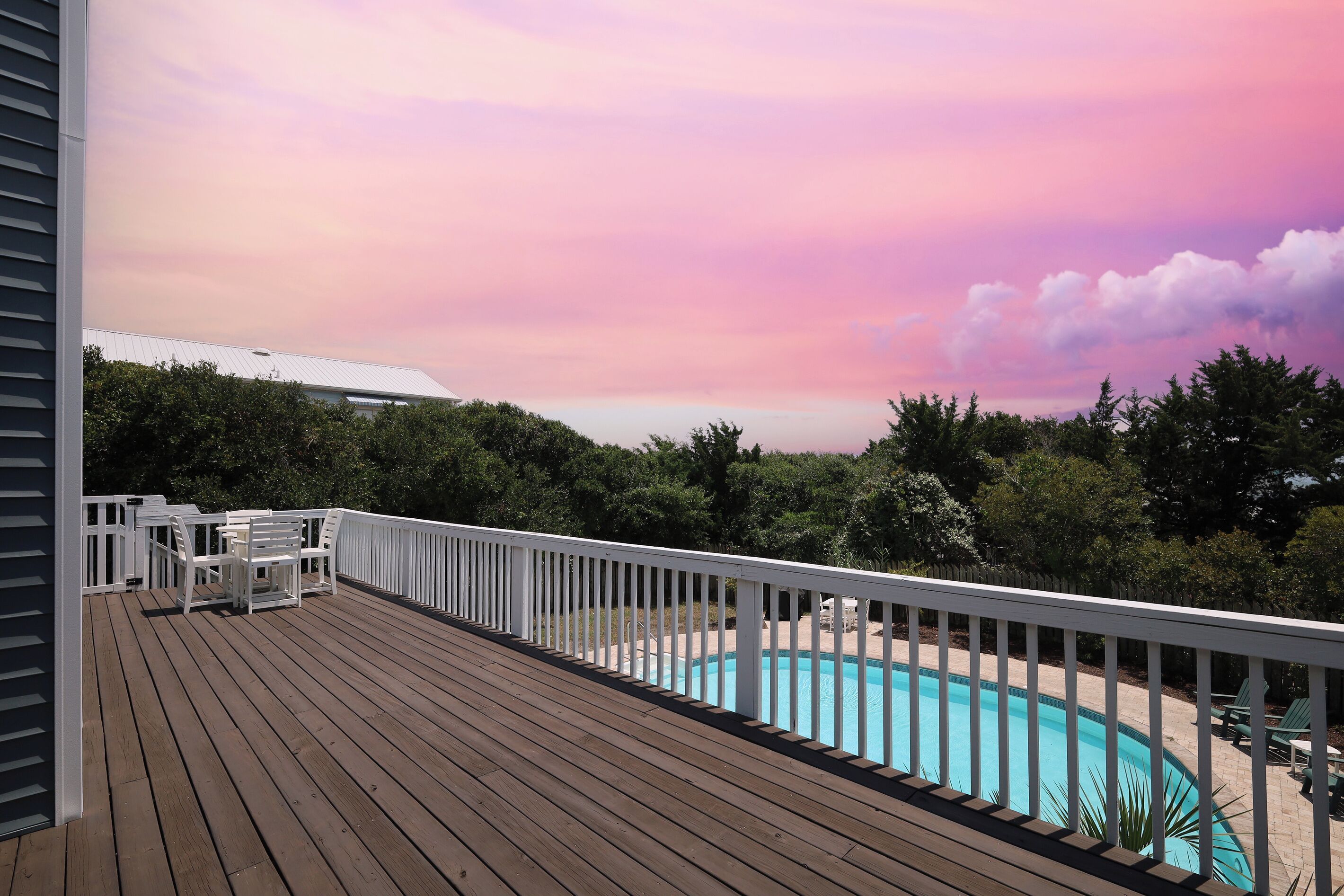 A wooden deck with a pool, surrounded by trees and a white fence.