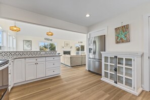 A spacious kitchen with white cabinetry, a central island, and a large refrigerator. - SeaEsta | Private Pool + 5 Min Walk to Beach (Emerald Isle)