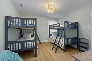Quarto com beliches, piso de madeira, luminária no teto e janela com persianas.