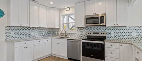 A modern kitchen with white cabinets, a stainless steel microwave, a dishwasher, and an oven.