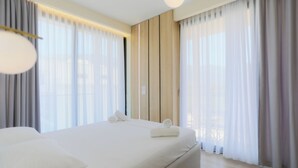 Una habitación de hotel moderna con una cama grande, paneles de madera y cortinas translúcidas.