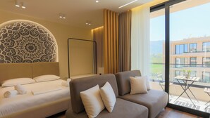 A modern hotel room with a sofa, a bed, and a large window offering a view of a building and greenery. - Modern Pool Side Studio Palm (Orikum)