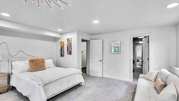 A bedroom with a bed, a sofa, a ceiling light fixture, and a door leading to another room.