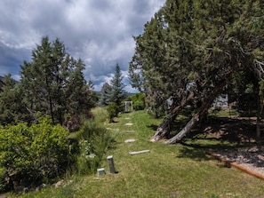 A pathway through a wooded area with a stone bench and a pergola.