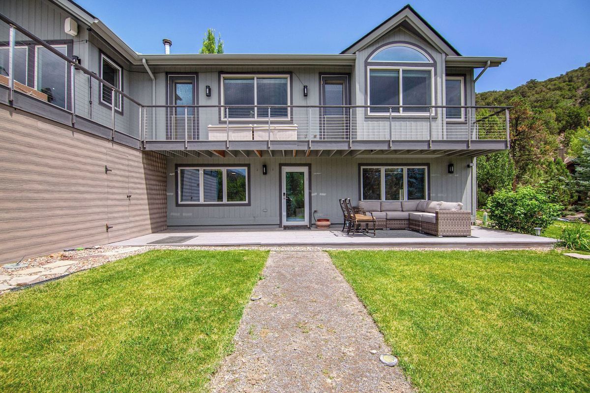 A two-story house with a covered patio, a stone pathway, and a grassy lawn.