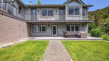 A two-story house with a covered patio, a stone pathway, and a grassy lawn.