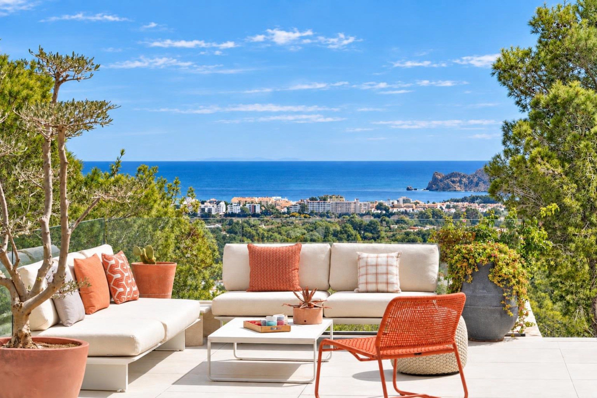A terrace with a sofa, chairs, and a table, overlooking a coastal cityscape.
