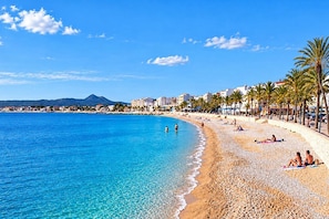 A beach with clear blue water, a sandy shore, and a row of palm trees. - Casa de Romero 6 pax - Javea, Costa Blanca (Javea)