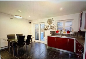 A modern kitchen with a dining area, featuring a red island, black chairs, and a glass door leading outside. - Rent my Sheffield City Home (Sheffield)