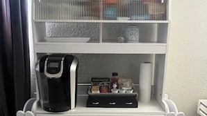 Un mini bar blanco con una cafetera, sobres de condimentos y una botella de agua.