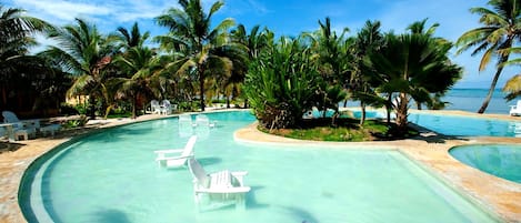 Ein Swimmingpool mit klarem Wasser, umgeben von Palmen und Liegestühlen.