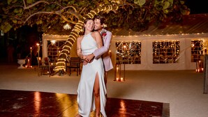 Una pareja abrazándose bajo un árbol con luces de cadena, una tienda de campaña con ventanas y un espacio para bailar.
