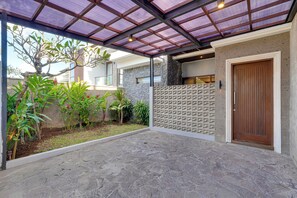 A covered outdoor area with a stone floor, a wooden door, and a wall with a geometric pattern. - Villa Eugene - Nusa Dua (Nusa Dua)