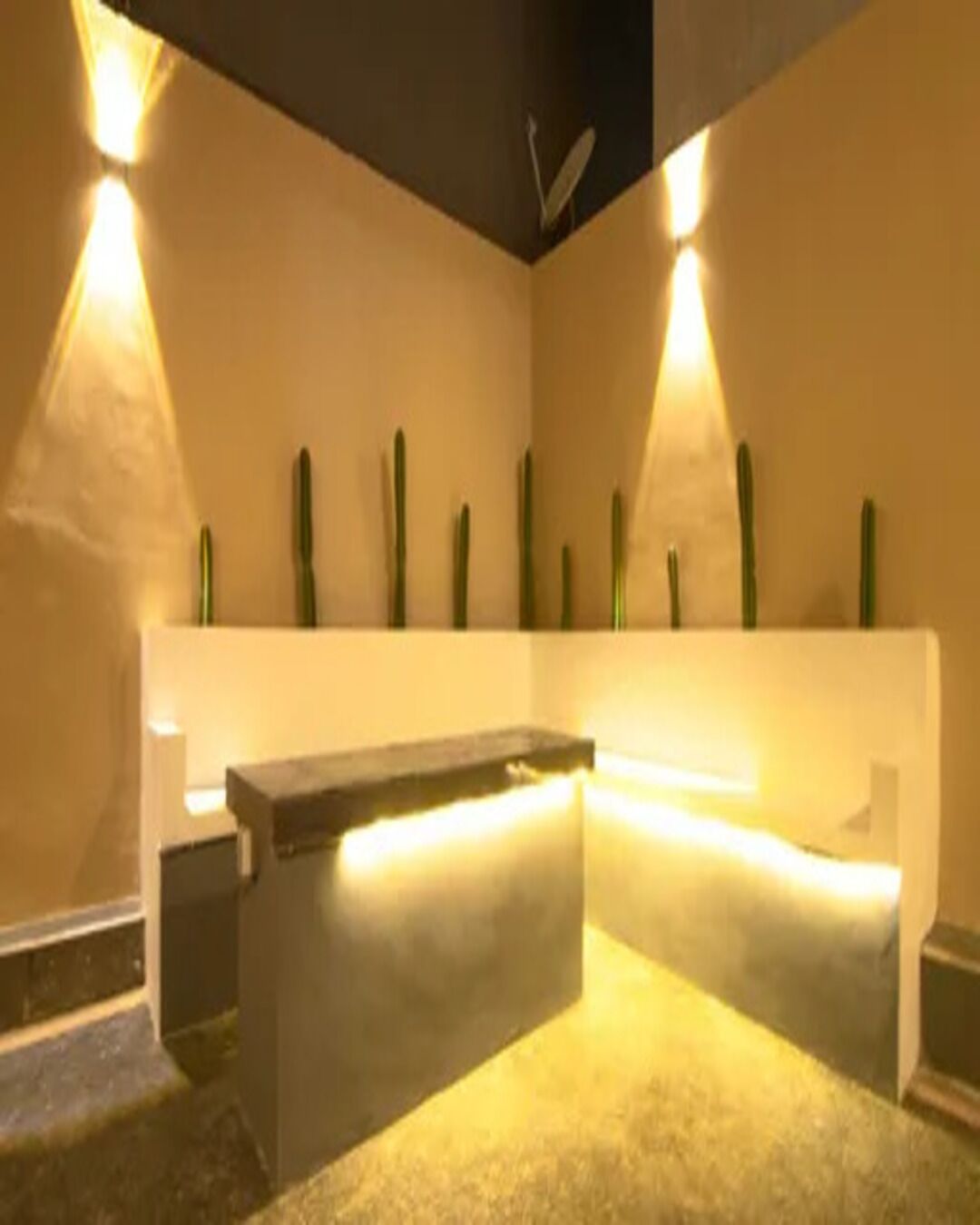 A reception desk with a bench, a wall-mounted plant, and two wall-mounted lights.