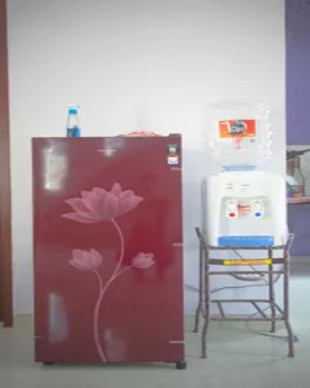 Un refrigerador con diseño floral, un dispensador de agua y una silla.