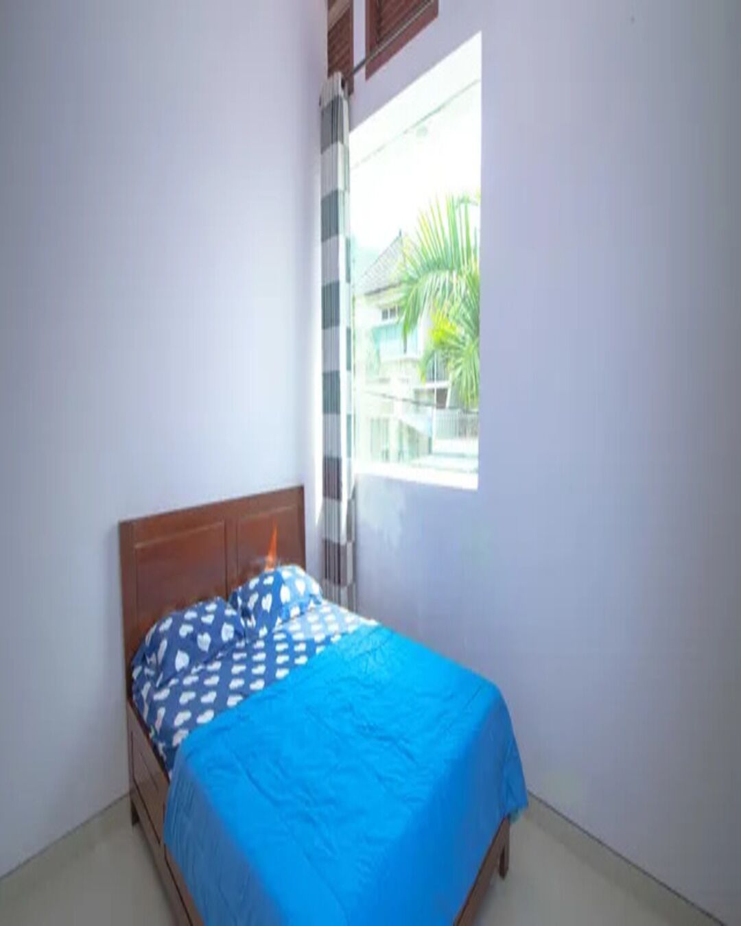 Un dormitorio con una cama individual, una ventana con persianas y vistas a un edificio.