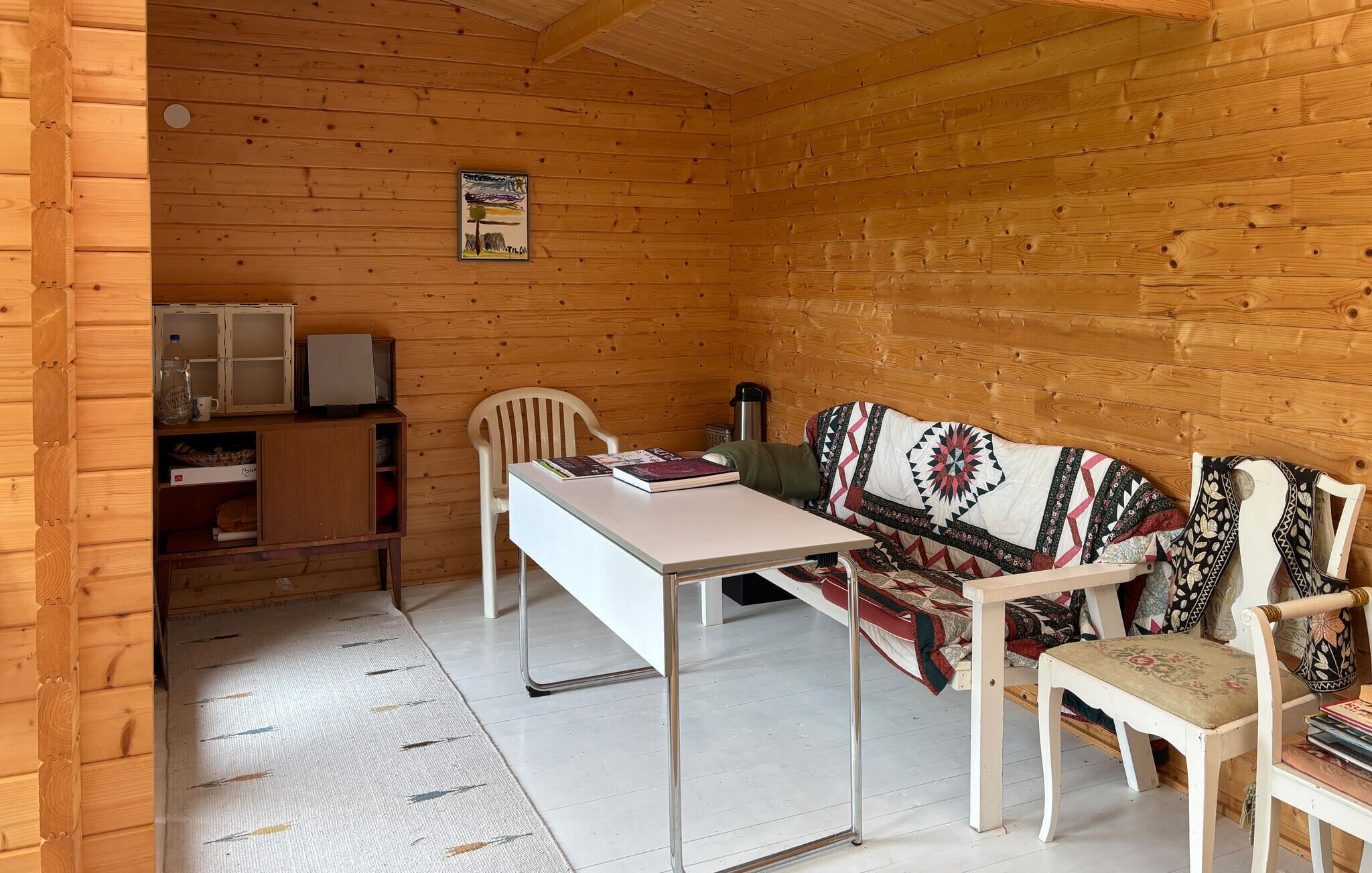 A wooden cabin interior with a dining table, chairs, a sofa, and a small kitchenette area.