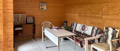 A wooden cabin interior with a dining table, chairs, a sofa, and a small kitchenette area.