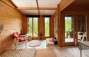 A wooden cabin interior with a bed, a bench, a table, and a view of the outdoors. - Cozy home in Ellös with sauna (Ellös)