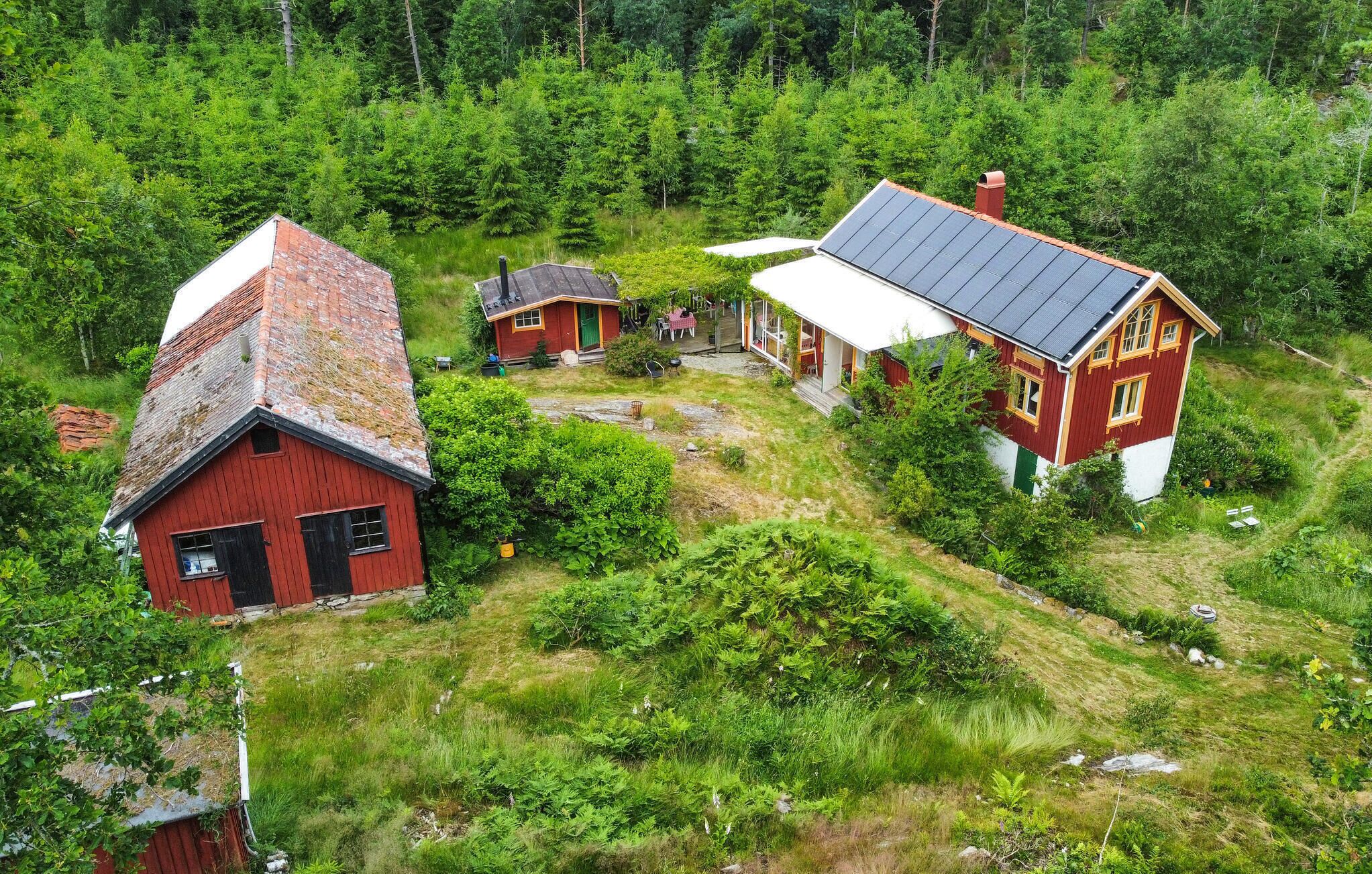 A red house with a sloped roof and a smaller adjacent building, surrounded by dense greenery and a pond.