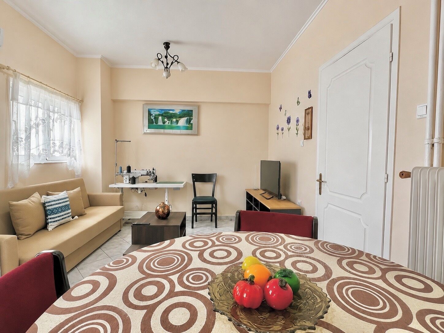 A living room with a sofa, a dining table with a decorative centerpiece, a sewing machine, a television, and a door.