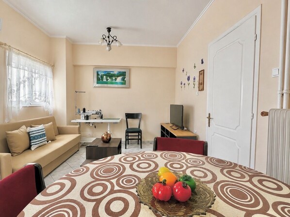 A living room with a sofa, a dining table with a decorative centerpiece, a sewing machine, a television, and a door. - Athens Lower Ground Gem - Near Metro by ΜΡS (Athina)