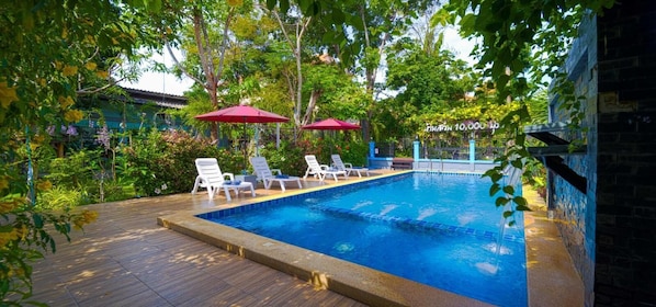 A swimming pool with lounge chairs and umbrellas, surrounded by greenery and a stone wall. - Fantastic resort    ,Where Every Stay Biossoms  into a Beautiful Memory. (อำเภอหัวหิน)