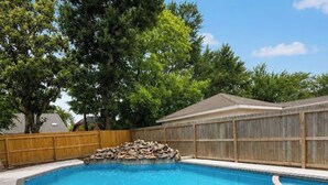 A swimming pool with a wooden fence, a covered area, and trees in the background. - Home in Bellaire (Bellaire)