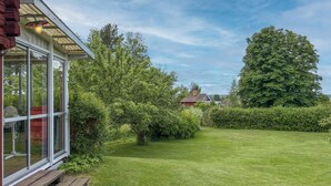Een verzorgd gazon met een houten bankje, een glazen constructie en een grote boom op de achtergrond.