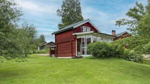Een rode houten woning met een glazen deuropening, omgeven door een verzorgd gazon en weelderige begroeiing.