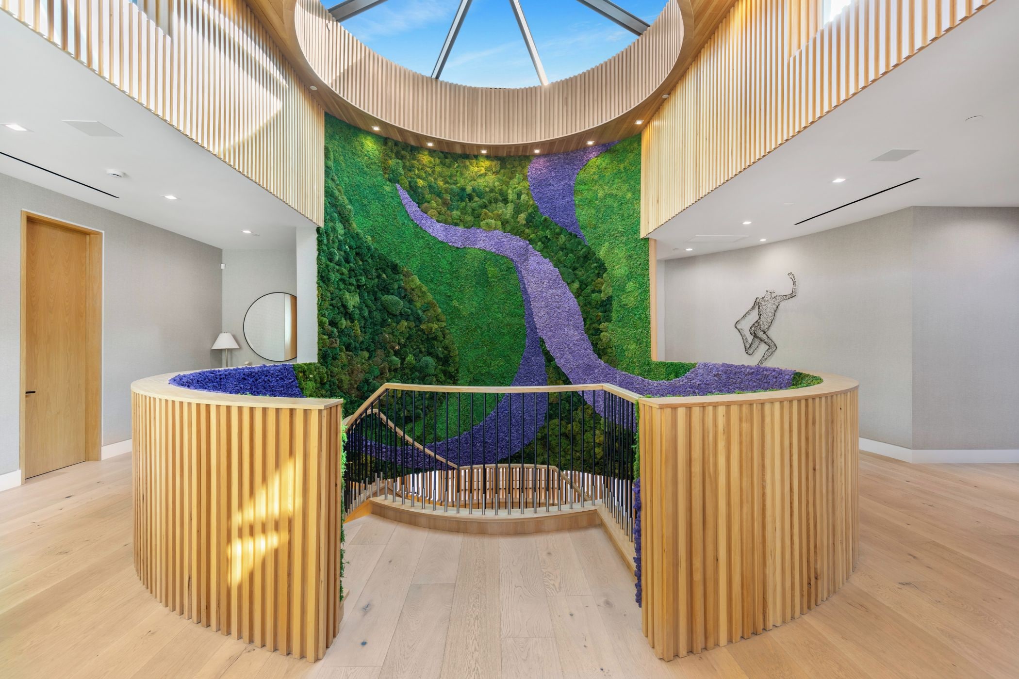 A modern reception area with a central staircase, wooden reception desk, and a green wall with a purple path.