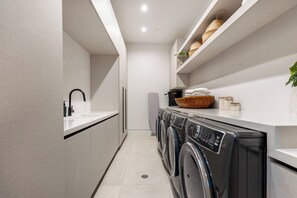 A modern laundry room with a washing machine, dryer, and a sink. - Somera Masterpiece (Los Angeles)