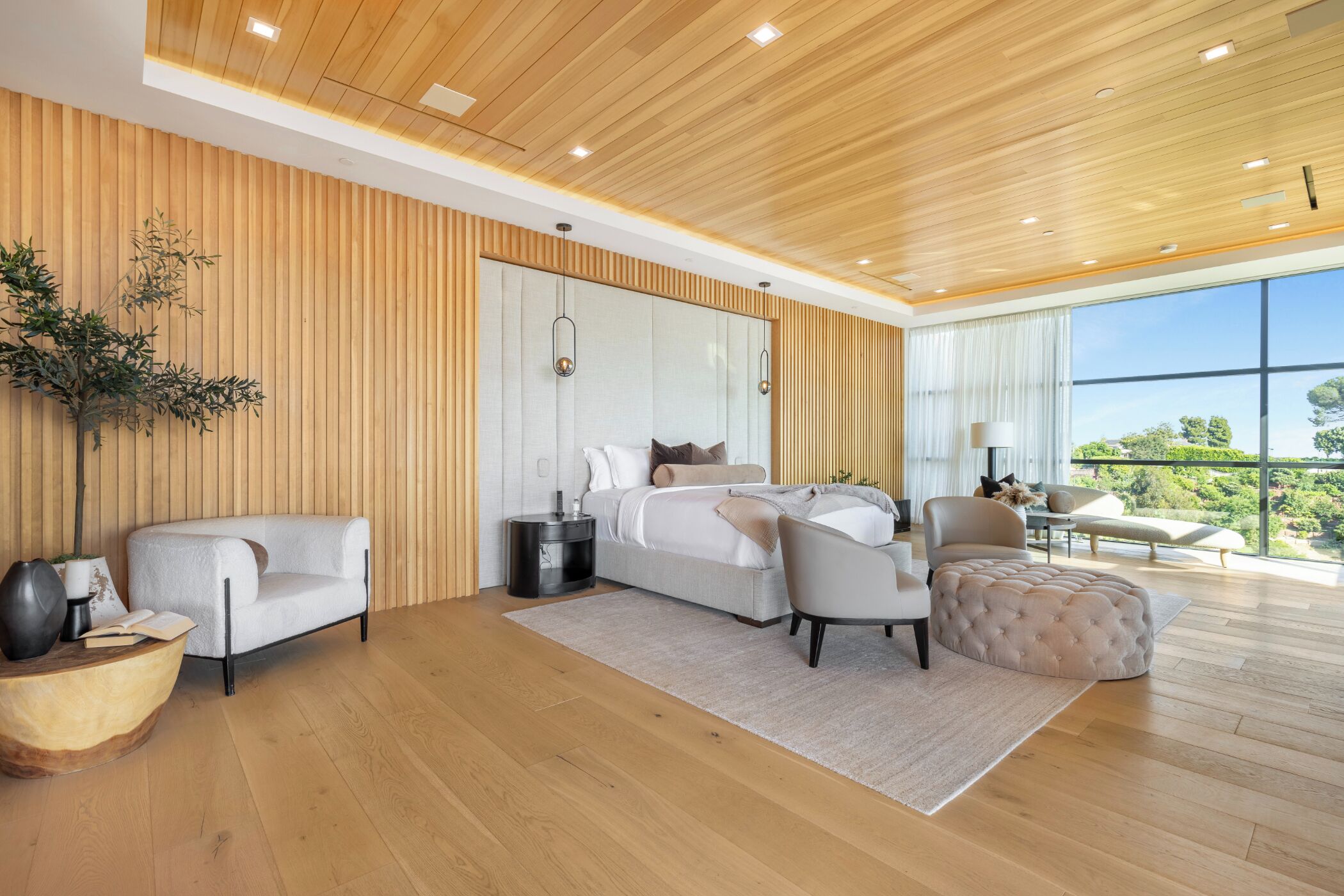 Une chambre à coucher moderne avec un grand lit, deux fauteuils, un canapé et une vue sur l’extérieur.