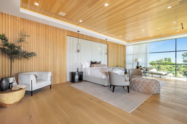 A modern bedroom with a large bed, two armchairs, a sofa, and a view of the outdoors.