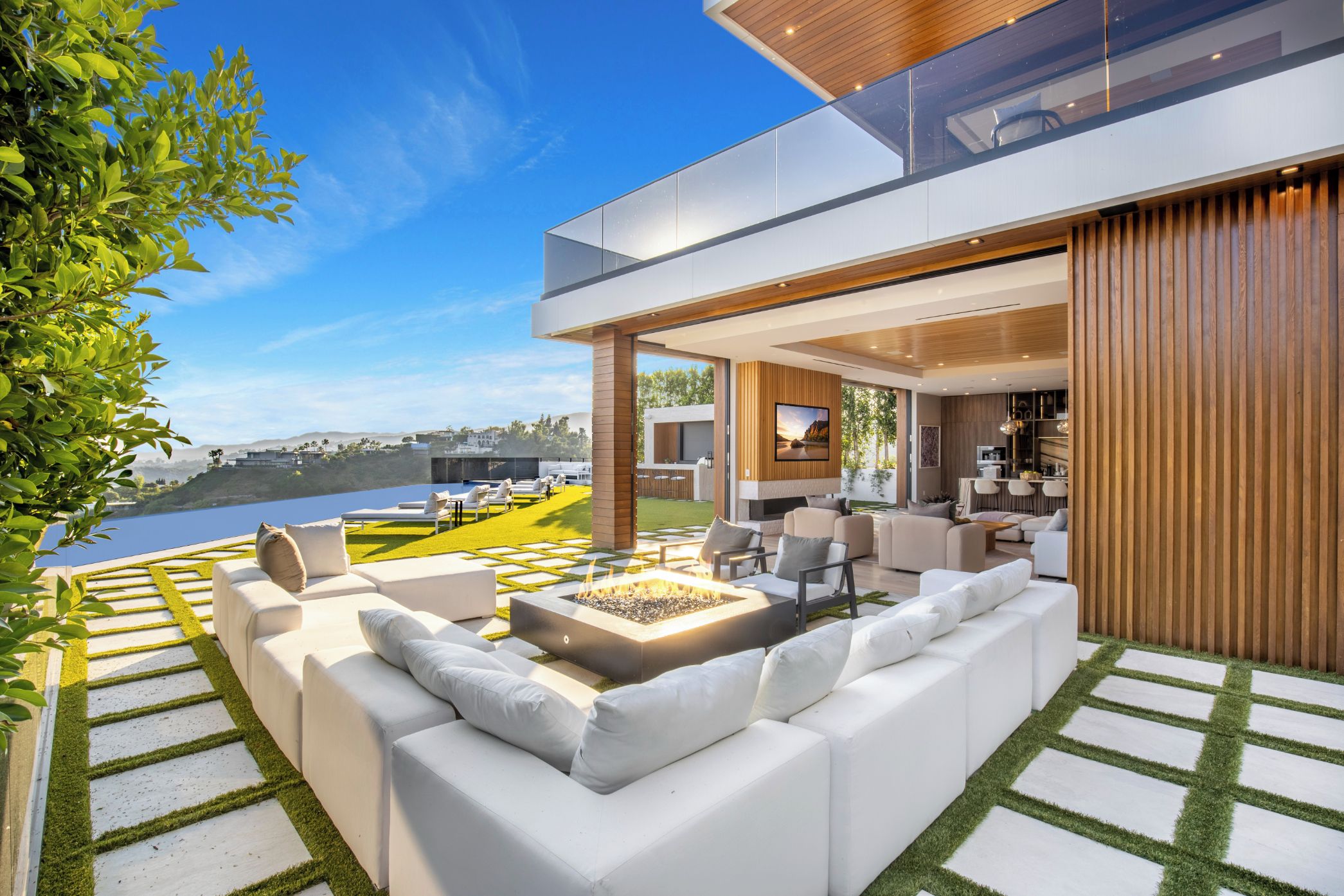 Un espace de vie extérieur moderne, doté d’un foyer, de canapés blancs et offrant une vue sur un plan d’eau.