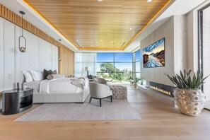 A modern bedroom with a large bed, bedside tables, a seating area, and a fireplace.