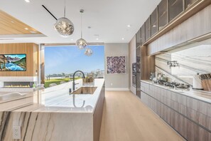 A modern kitchen with a large island, wooden cabinetry, and a view of the outdoors.