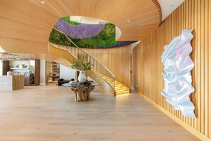 A modern interior with a wooden staircase, a unique ceiling design, and a central plant display. - Somera Masterpiece (Los Angeles)