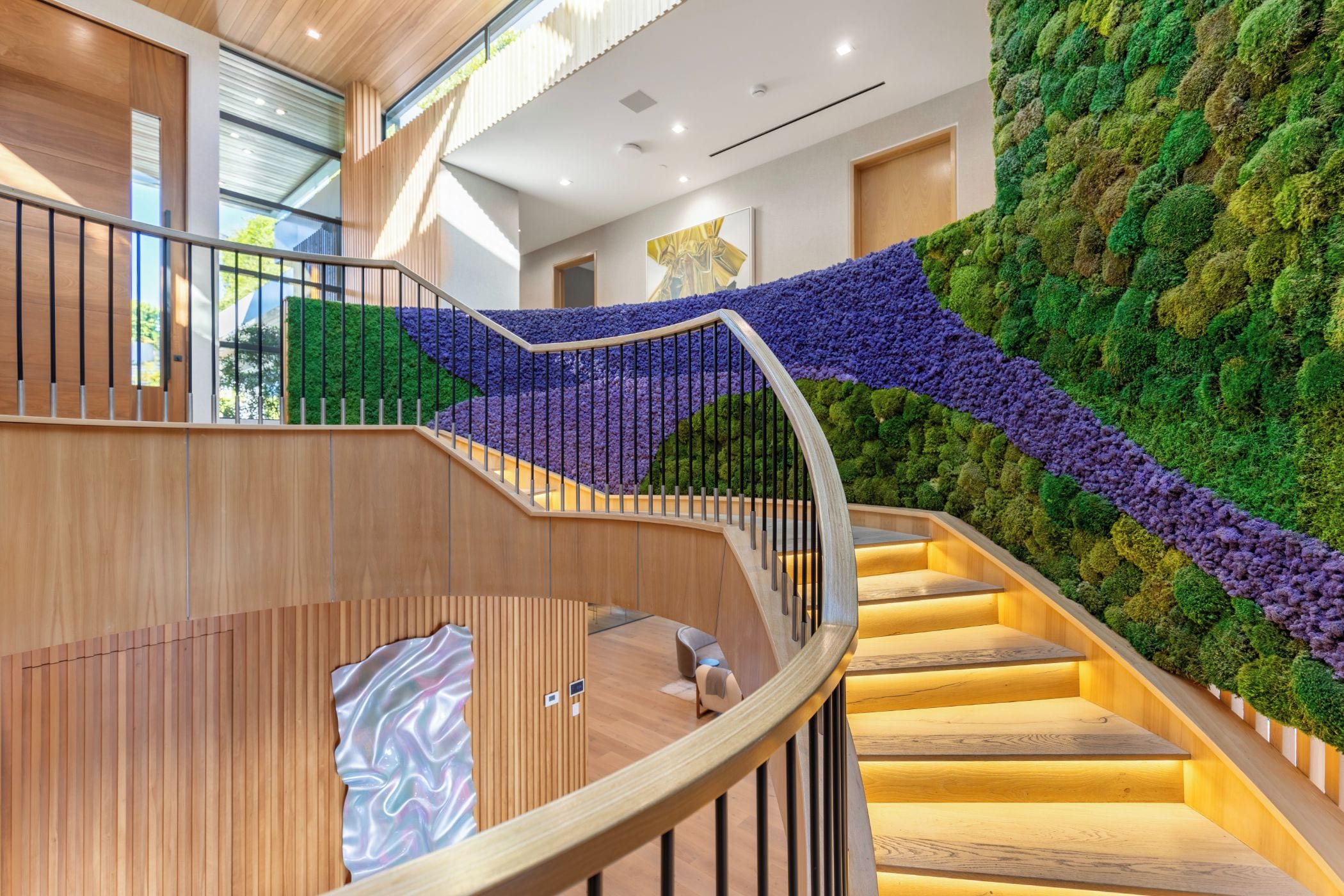Un interior moderno con una escalera curva, suelo de madera y una pared cubierta de musgo verde.
