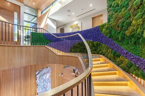 A modern interior with a curved staircase, wooden flooring, and a green moss wall. - Somera Masterpiece (Los Angeles)