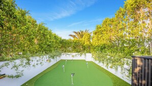 A miniature golf course with a green artificial turf, surrounded by lush greenery and trees.