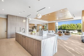 A modern kitchen with a marble island, wooden cabinets, and pendant lighting. - Somera Masterpiece (Los Angeles)