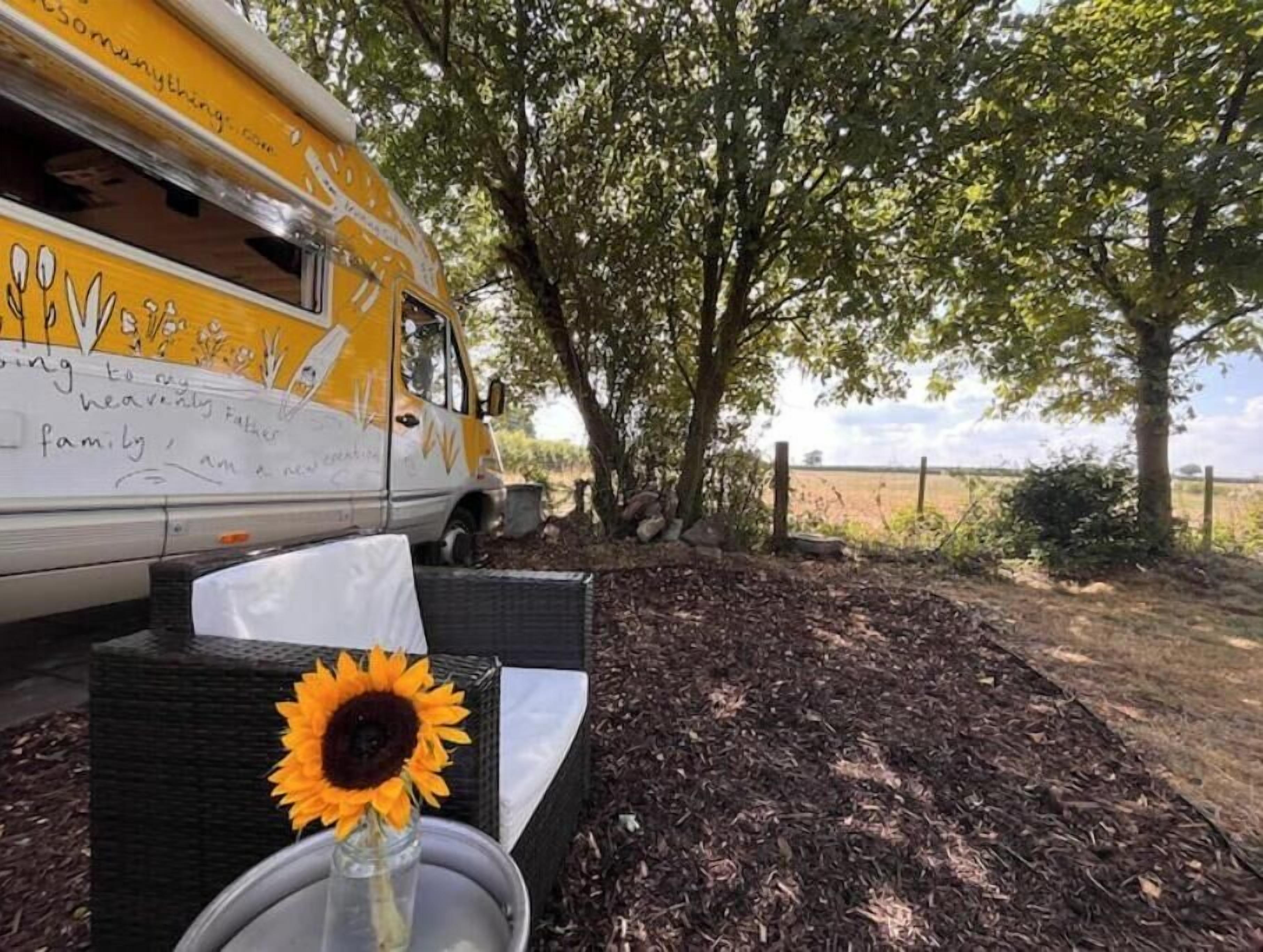A yellow vehicle with handwritten text, a sunflower, and a wicker chair in a natural setting.