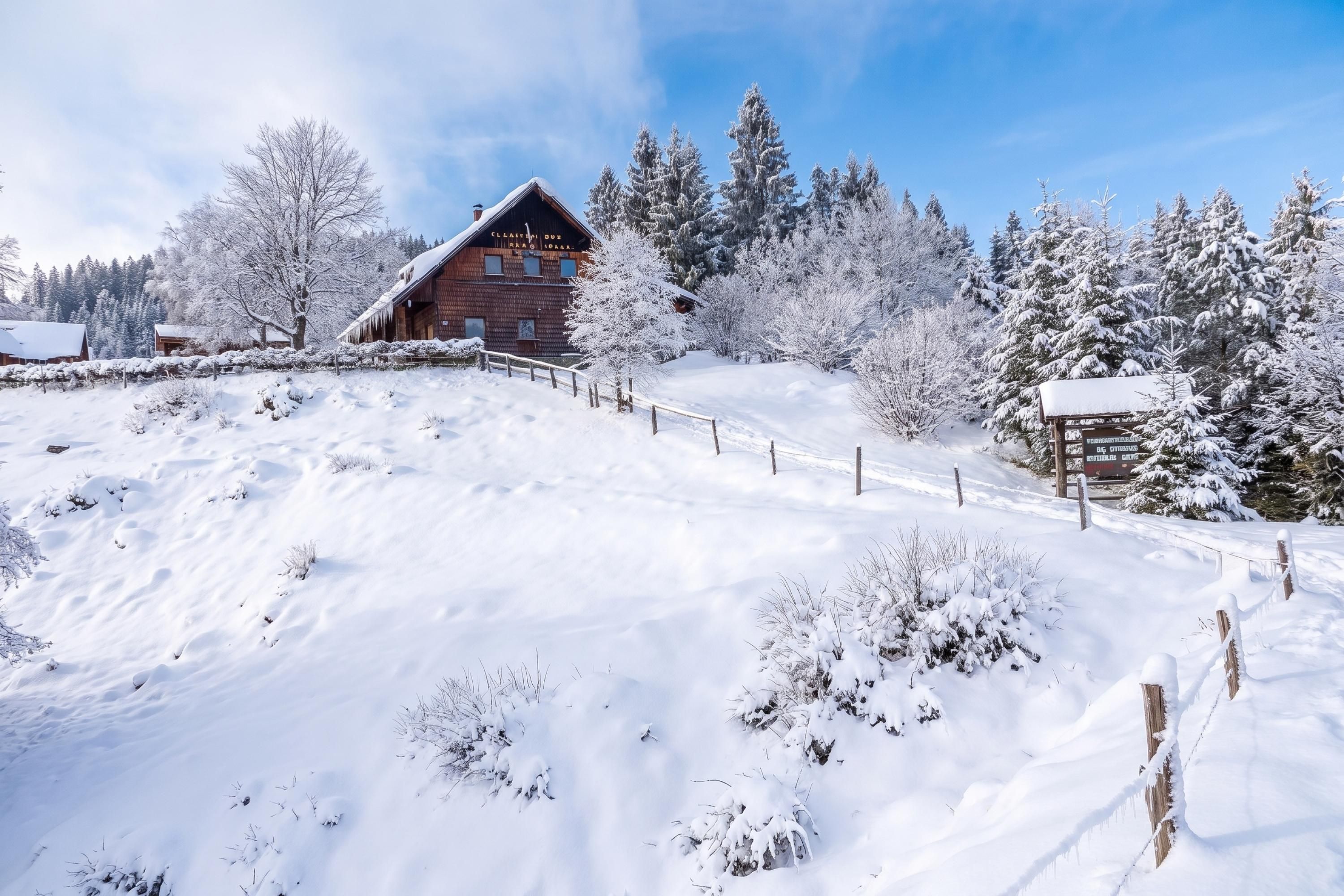 A wooden cabin with a sloped roof, surrounded by snow-covered trees and a clear sky.